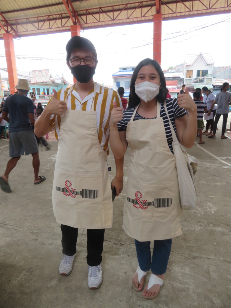 Lance and Tricia wearing Spatula&Barcode logo aprons and giving a thumbs up to the camera.