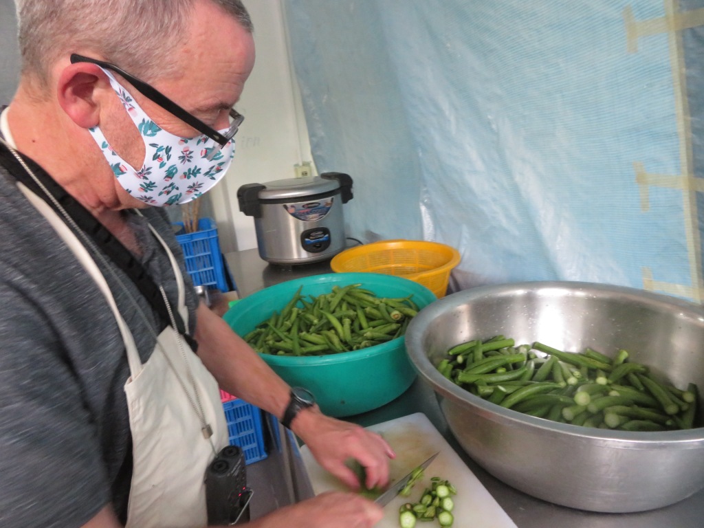 Michael in a patterned face mask chopping okra with two large bowls of okra in the background