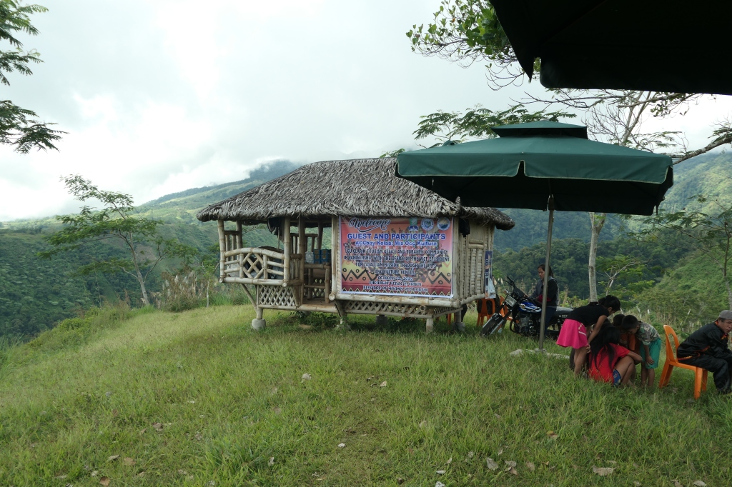 a thatched building with a welcome banner attached, mountains in the background